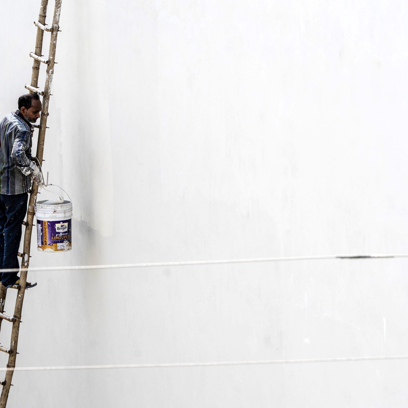 Peintre sur une échelle qui passe un rouleau sur un grand mur blanc